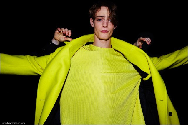 Photograph of male model Charlie James putting on a Devon Halfnight Leflufy men's coat, backstage at the Fall/Winter 2016 show. Photography by Alexander Thompson for Ponyboy magazine.