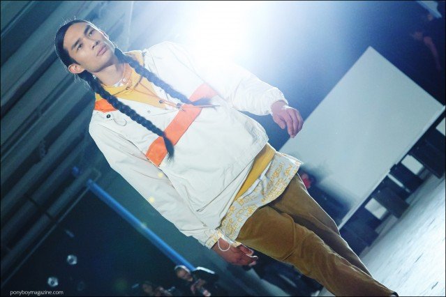 A long-haired male model in braids walks the runway for Rochambeau F/W16 menswear show. Photography by Alexander Thompson for Ponyboy magazine.