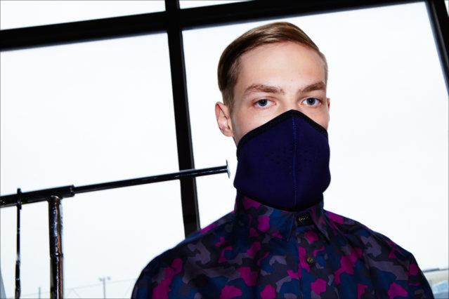 A male model photographed in a face mask and camo shirt, backstage at Robert Geller A/W17 menswear show. Photography by Alexander Thompson for Ponyboy magazine NY.