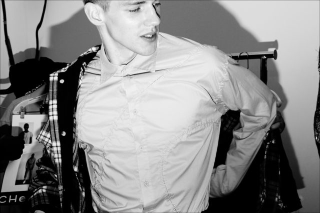 A male model snapped getting dressed, backstage at the Feng Chen Wang menswear show. Photographed by Alexander Thompson for Ponyboy magazine.