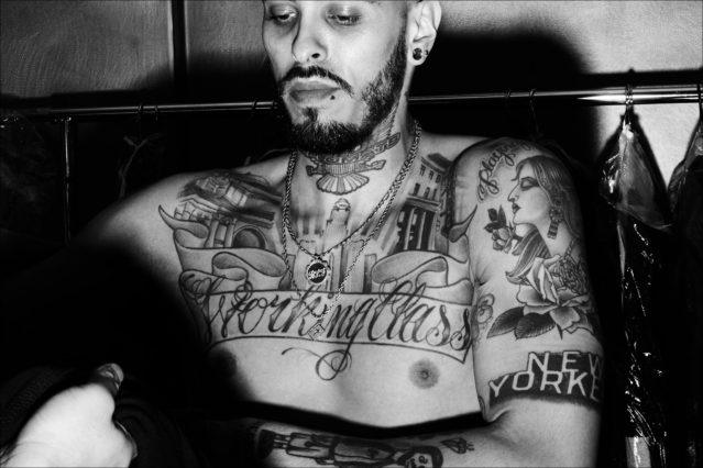 A heavily tattooed model snapped backstage dressing at Willy Chavarria menswear show for Fall 2018. Photography by Alexander Thompson for Ponyboy magazine.