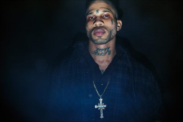 A model with face tattoos and crucifix poses backstage at the Willy Chavarria menswear show. Photography by Alexander Thompson for Ponyboy magazine.